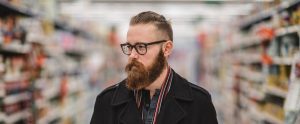 a hipster with a beard and glasses in a supermarket aisle