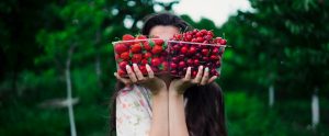 a woman holding two plastic containers of strawberries and cherries in front of her face