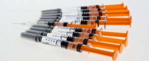 group of unopened syringes lying on white surface, and one opened syringe