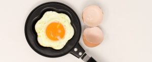 a frying pan with a cracked egg in it and the egg shells lying next to it