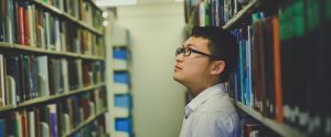 Asian man standing against a bookshelf in a library