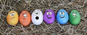 six colourful eggs with cartoon faces drawn on them in hay