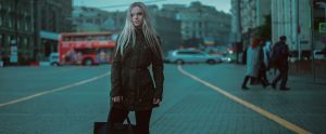 a blonde woman standing on a British street holding a bag