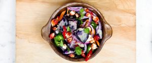 a bowl of vegetable salad on a wooden tray