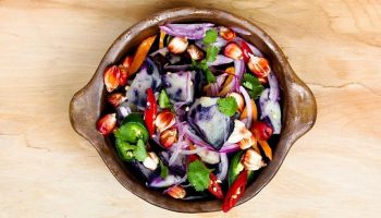 a bowl of vegetable salad on a wooden tray
