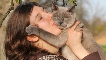 a woman holding and kissing a gray cat