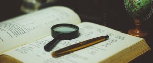 an open book with a magnifying glass and pen on top of it