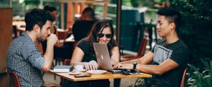 three young adults on a desk around a MacBook Pro