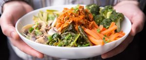 a person holding a bowled meal of vegetables