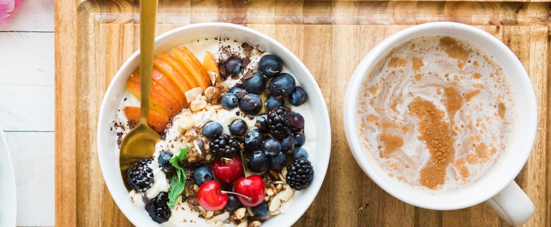 breakfast bowl of porridge with berries next to a coffee on a cutting baord