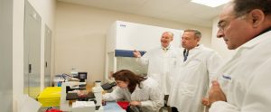 researchers in white lab coats around a microscope