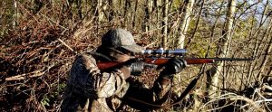 a man in camouflage gear aiming a hunting rifle