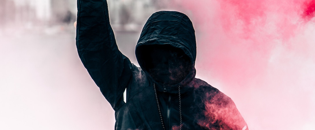 a radical in a black hoodie with red mist around him