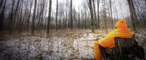 hunter in high visibility uniform sitting in a hunting chair in the woods waiting for prey
