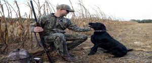 hunter in camo with a rifle petting his hunting dog