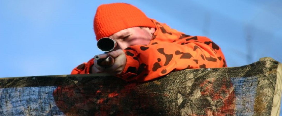 hunter in high visibility coat aiming a rifle
