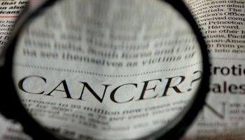 a magnifying glass hovering the word "cancer" in a newspaper