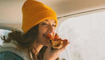 woman with a yellow hat eating a pizza