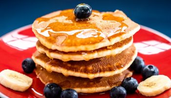 pancakes with maple syrup, bananas and blue berries on a red plate