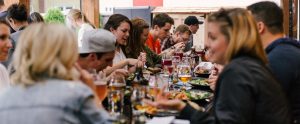people eating and drinking on a long table at a restaurant