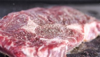 uncooked salted red meat being cooked in a frying pan with olive oil