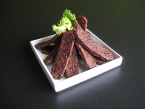 slices of tempeh bacon artfully arranged and garnished on a square white plate