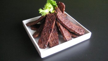 slices of tempeh bacon artfully arranged and garnished on a square white plate