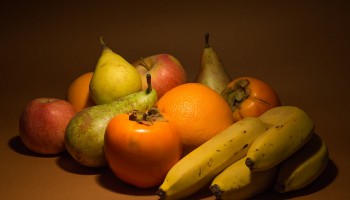 various fruits grouped together and softly lit on a brown surface