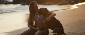 a woman in a bikini sitting with her boxer on the beach