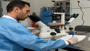 researcher looking into a microscope and writing on a paper