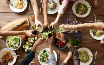 group of people having meal together clinking glasses over table