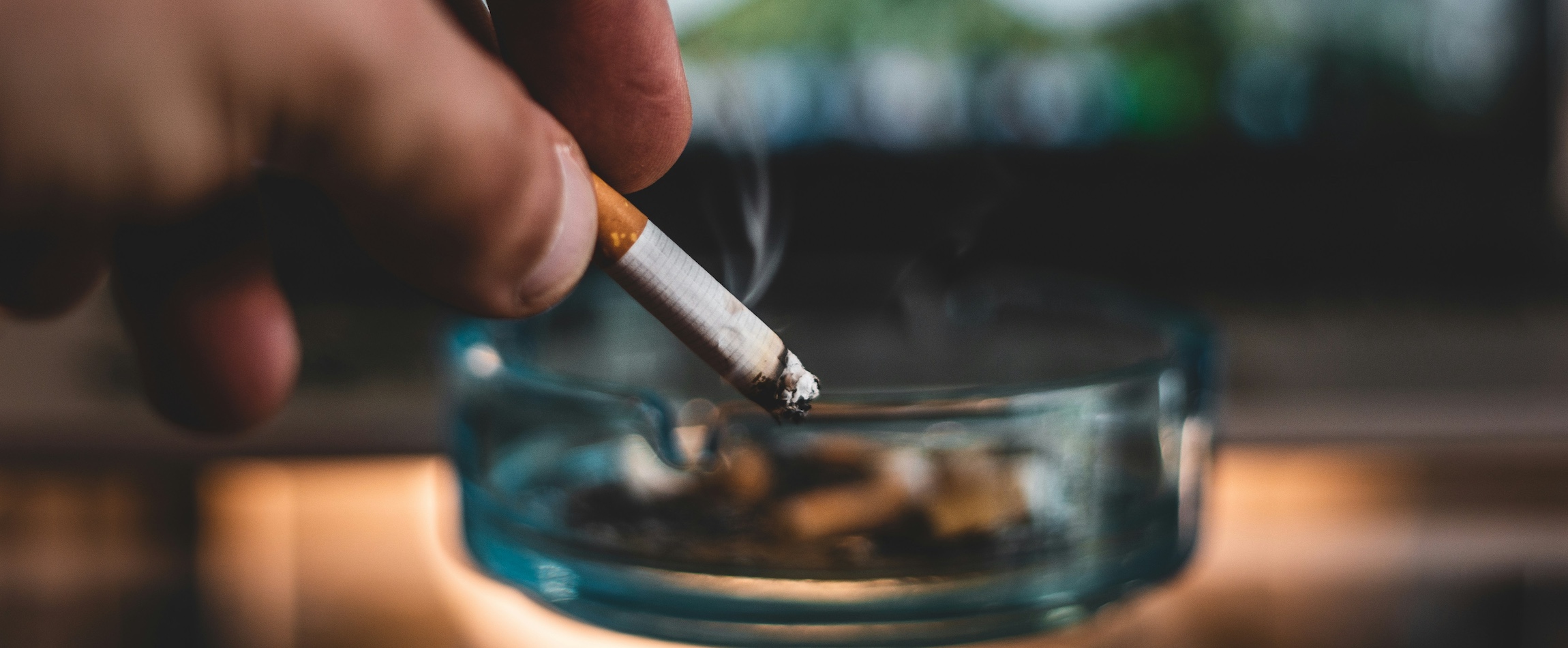 hand holding a cigarette near an ashtray