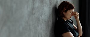 person with headache leaning against wall