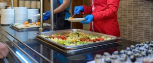 two people serving food at buffet-style cafeteria