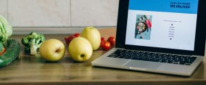 laptop on counter next to fruits and vegetables online grocery shopping