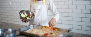child wearing apron making veggie pizza