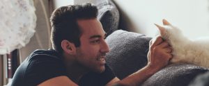 man sitting on couch petting white cat