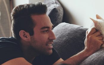 man sitting on couch petting white cat