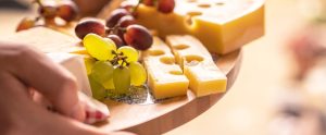 hands holding wooden board with cheese and grapes