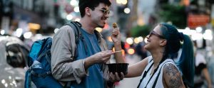 two friends outdoors sharing street food and laughing
