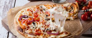 cheesy slice of pizza being lifted off wooden board