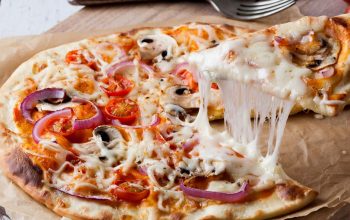 cheesy slice of pizza being lifted off wooden board