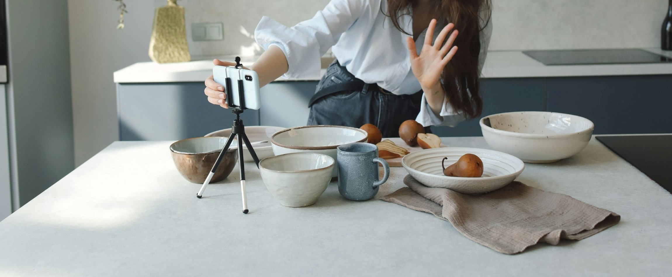 person waving at phone with bowls on kitchen counter
