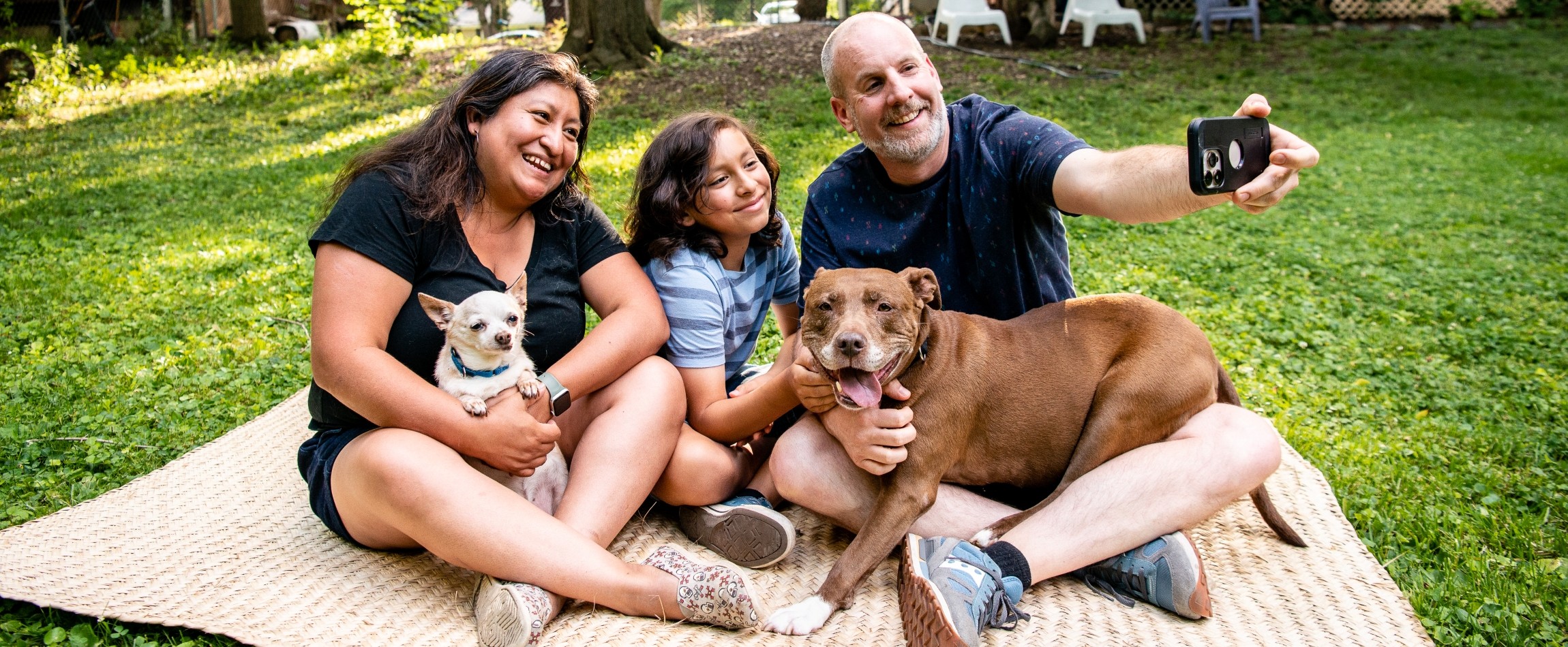 family outdoors sitting on blanket with two dogs taking photo