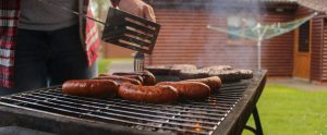 close-up of hands grilling sausages on barbeque
