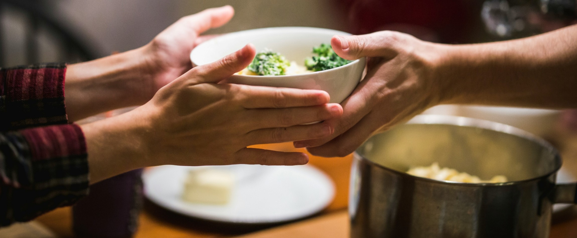 close-up of hands passing bowl of food over dinner table