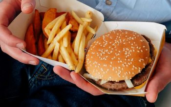close-up of hands holding fast food container with burger and fries