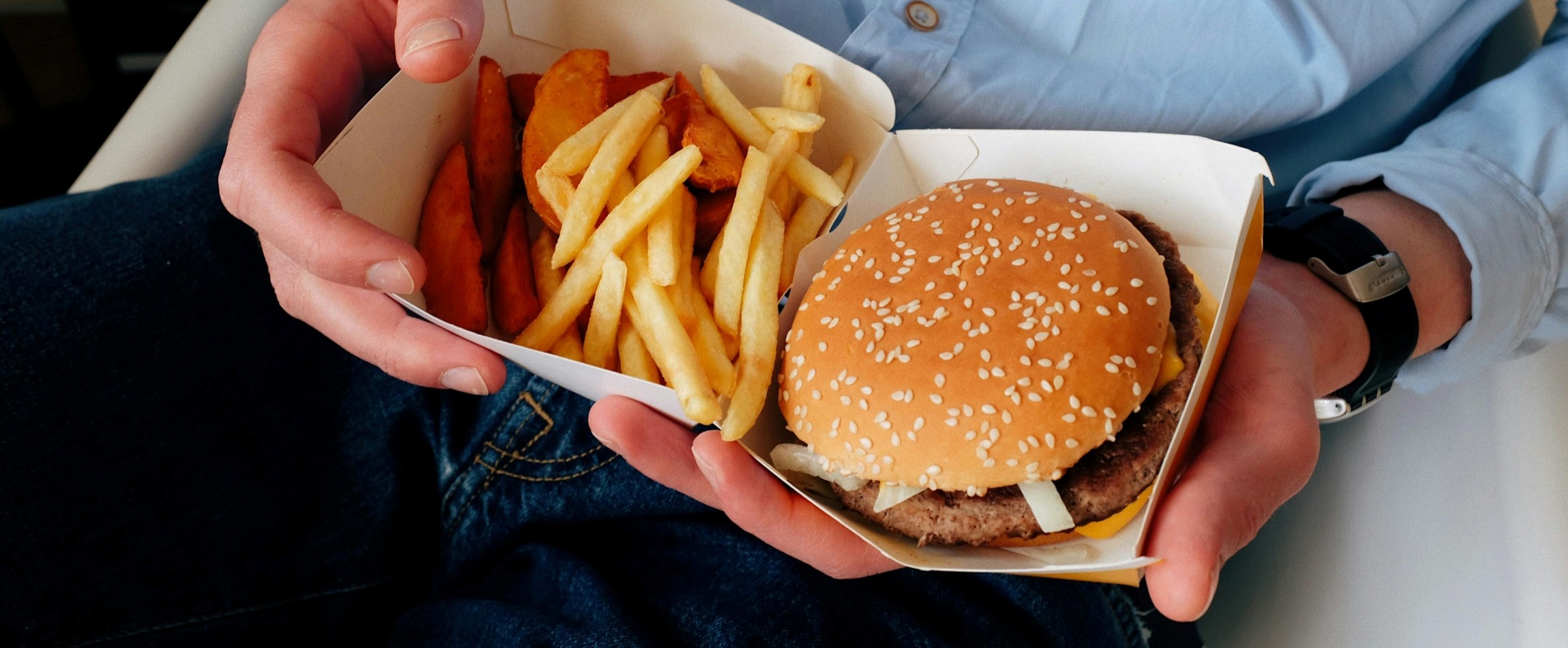 close-up of hands holding fast food container with burger and fries