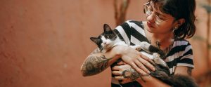 person with tattooed arms holding young black-and-white cat