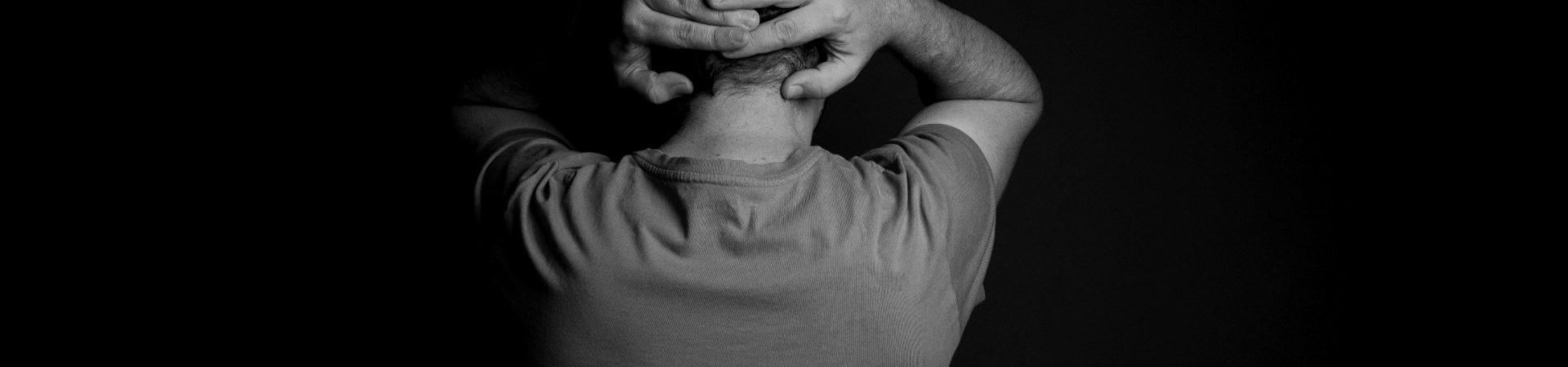 person with hands clasped behind head back turned to camera black and white